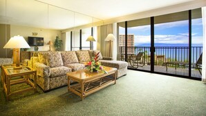 A hotel room with a sofa, two armchairs, a coffee table, and a balcony with a view of the ocean.