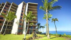 A multi-story hotel with balconies, palm trees, and a view of the ocean.