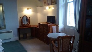 Una habitación con escritorio, silla, cama, cómoda y ventana.