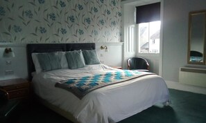 Une chambre à coucher avec un lit, une table de chevet, une chaise, une fenêtre et un miroir.