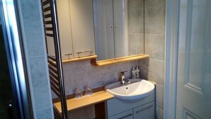 Un baño moderno con cabina de ducha de vidrio, un lavabo blanco y un mueble de tocador con espejo.