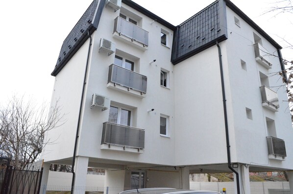 Un edificio de varios pisos con balcones, unidades de aire acondicionado y una entrada con portón.