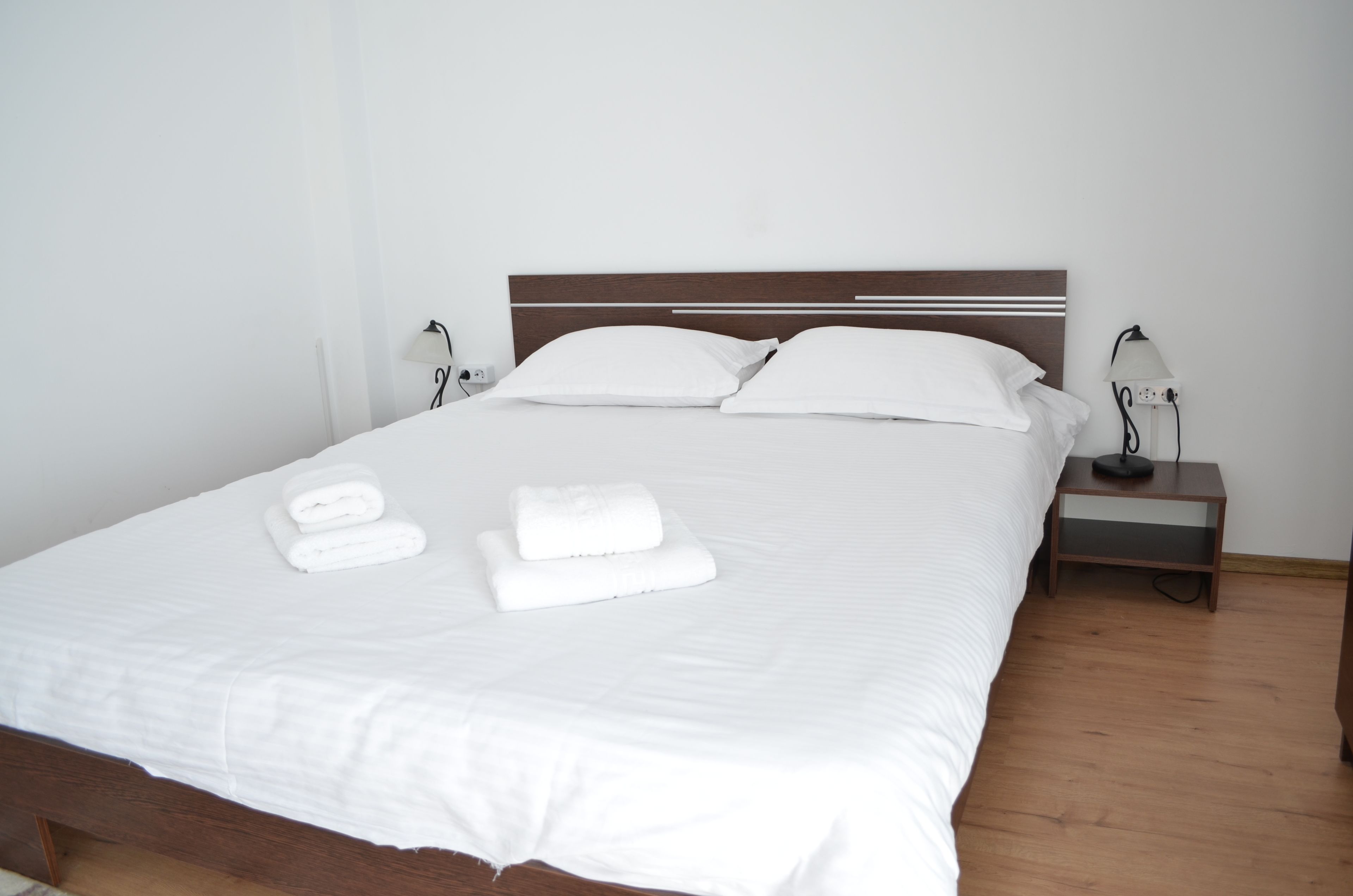 Un lit bien fait, avec du linge de lit et des serviettes blanches, une tête de lit en bois et des lampes de chevet posées sur une table de chevet en bois.