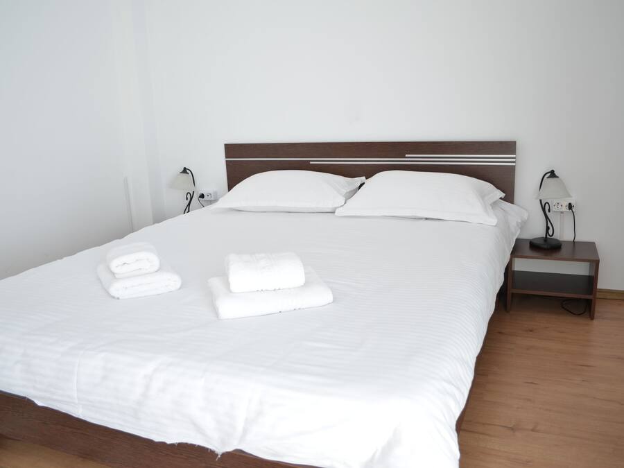 A neatly made bed with white linens and towels, a wooden headboard, and bedside lamps on a wooden nightstand.