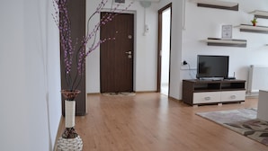 A modern living room with a wooden floor, a dark wooden door, a white wall, a TV stand, and a decorative vase. - Alexys Residence 8 (Iasi)