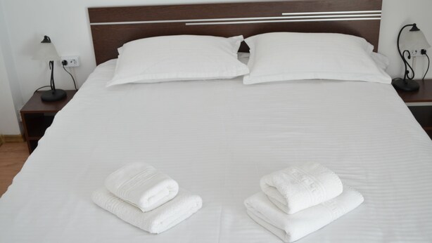 A neatly made bed with white linens and two folded towels on the bed. - Alexys Residence 8 (Iasi)