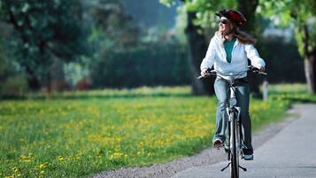 Una persona montando en bicicleta por un sendero pavimentado en un parque con césped y flores amarillas.