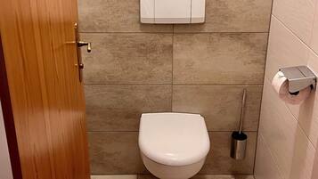 Un baño pequeño con un inodoro, un dispensador de papel higiénico y un secador de manos.