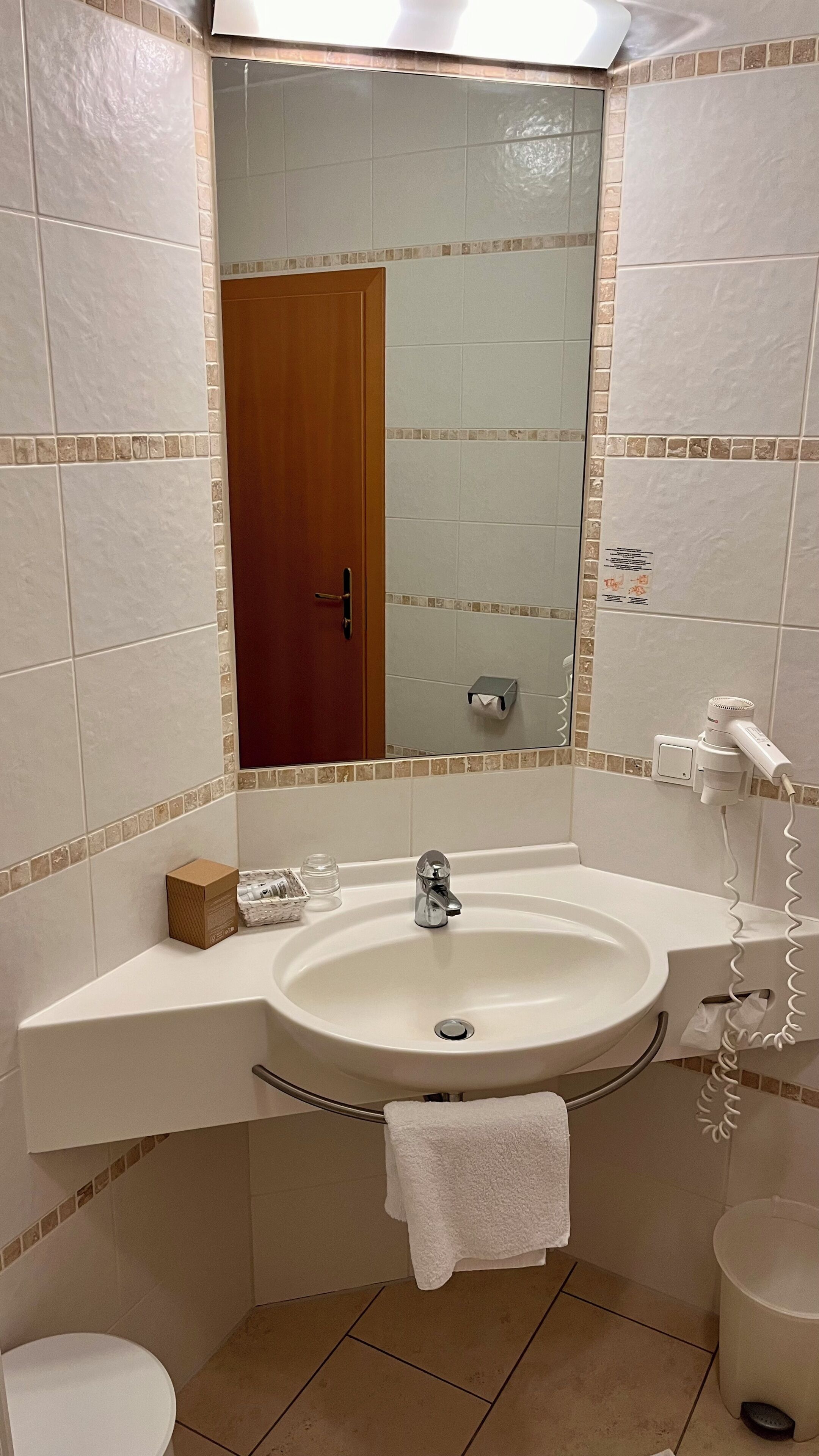 A bathroom with a sink, mirror, toilet, and a hairdryer plugged in.