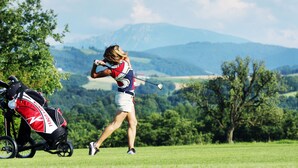 Un golfista con un atuendo rojo y blanco en un campo de golf, cerca de un bolso de golf rojo y blanco.