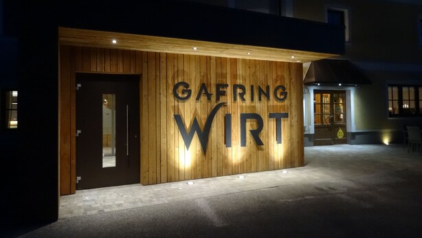 Fachada de edificio con el nombre "GAERING WIRT" iluminado sobre un panel de madera.