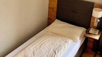 Een eenpersoonsbed met houten hoofdeinde, een nachtkastje met een lamp en een telefoon.