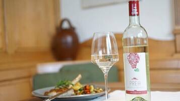 A bottle of white wine and a glass on a table with a plate of food.