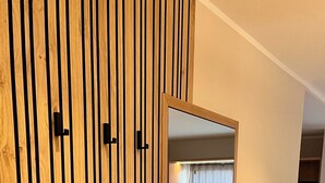 Una habitación con separador de listones de madera, puerta de armario espejada, radiador, cama y ventana con cortinas.