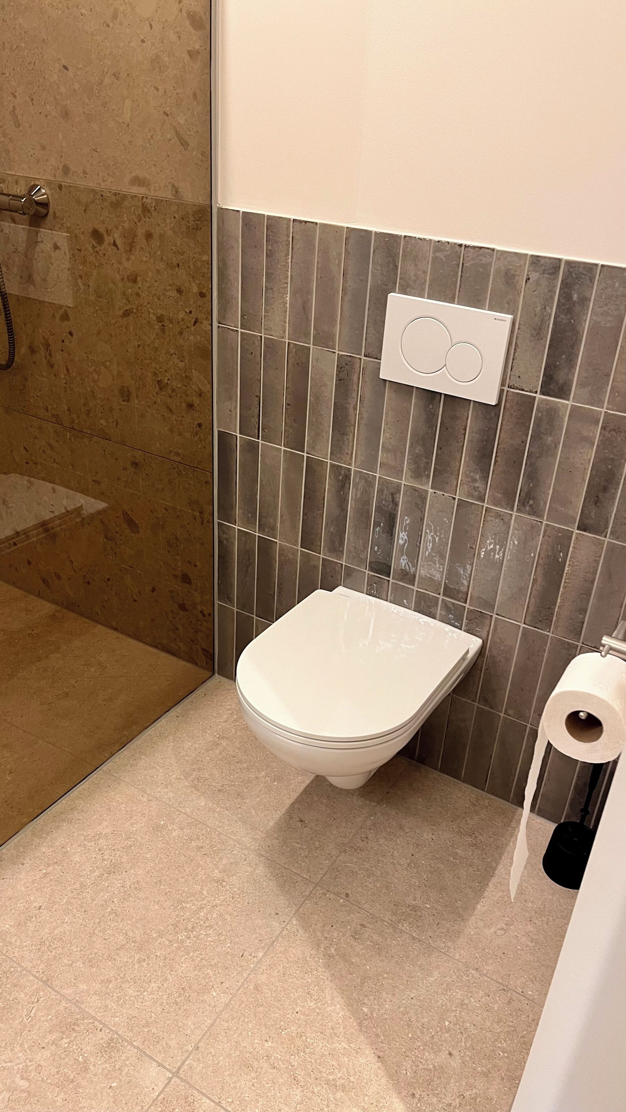 Un baño con inodoro, ducha y dispensador de papel higiénico en la pared.