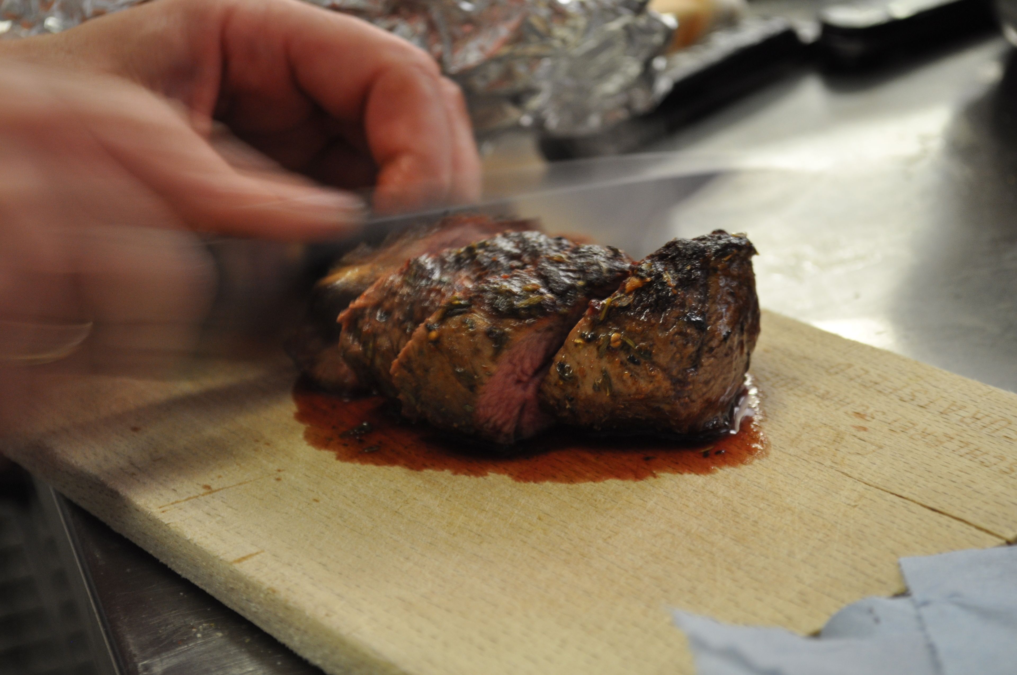 A person slicing a cooked meat on a wooden cutting board.