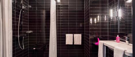 A modern bathroom with dark tiles, a shower, a sink with a mirror, and two towels on the wall.