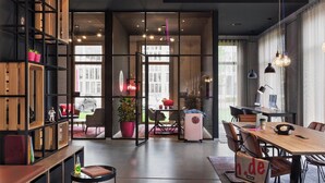 A modern interior with a wooden dining table, chairs, a bookshelf, and a large window. - Moxy Darmstadt (Darmstadt)