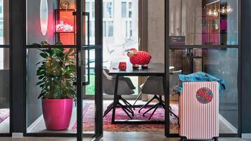 A modern interior with a glass partition, a potted plant, a table with chairs, a suitcase, and a neon sign.