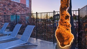 A courtyard with a large rock sculpture, a brick building, and a parking area.