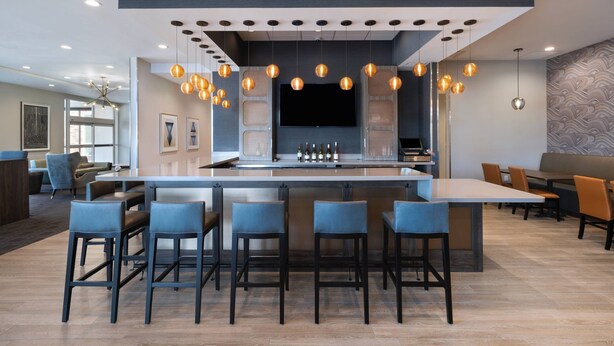 A modern bar area with a central island, bar stools, hanging pendant lights, and a flat-screen TV.