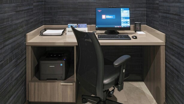 Ein moderner Arbeitsraum mit Wandverkleidung aus dunklem Holz, einem Schreibtisch mit Computer, einem Stuhl und einem Drucker.