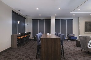 Une salle de conférence avec une longue table, des chaises et un petit coin salon comprenant un canapé et des fauteuils.