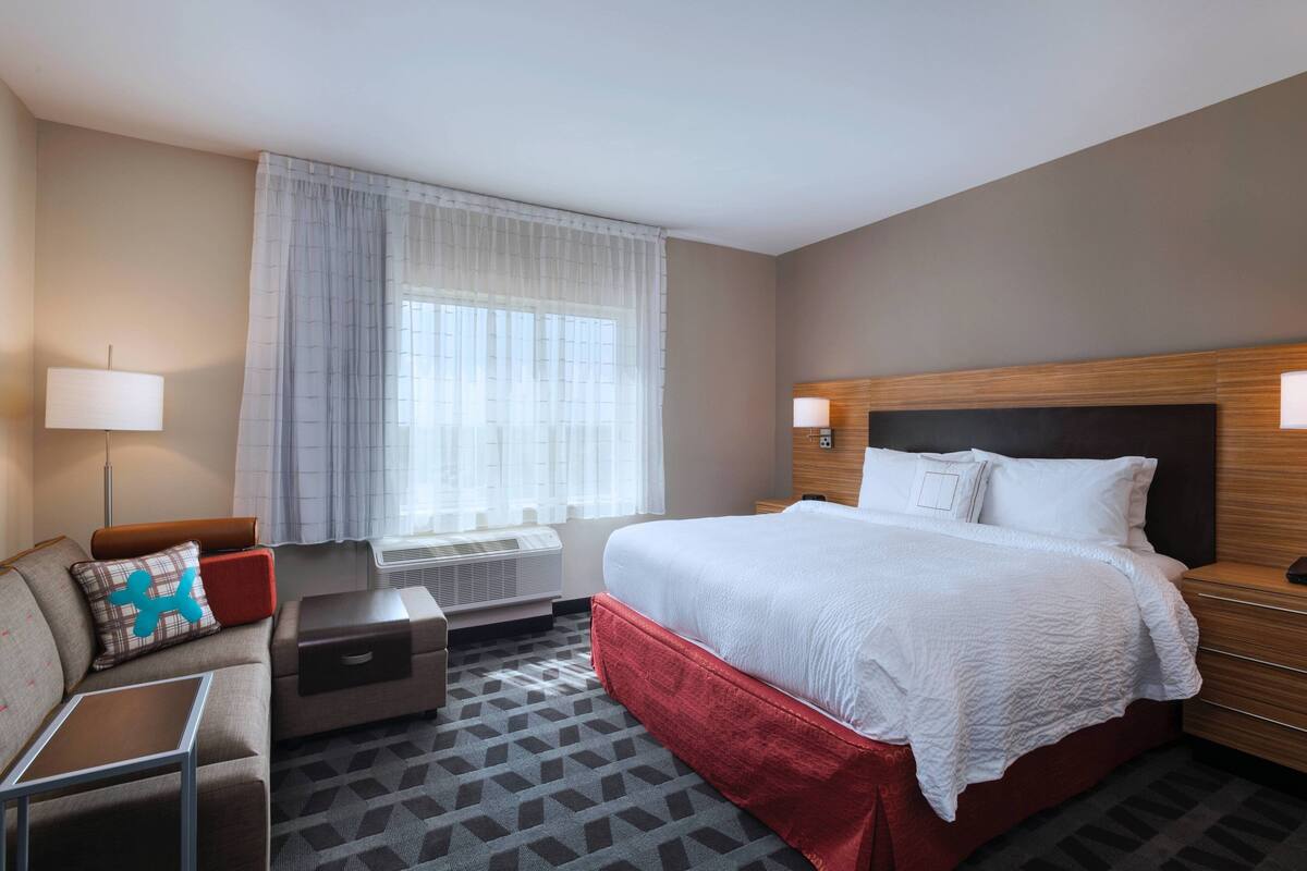 Ein Hotelzimmer mit Bett, Sofa, kleinem Tisch und einem Fenster mit Vorhängen.