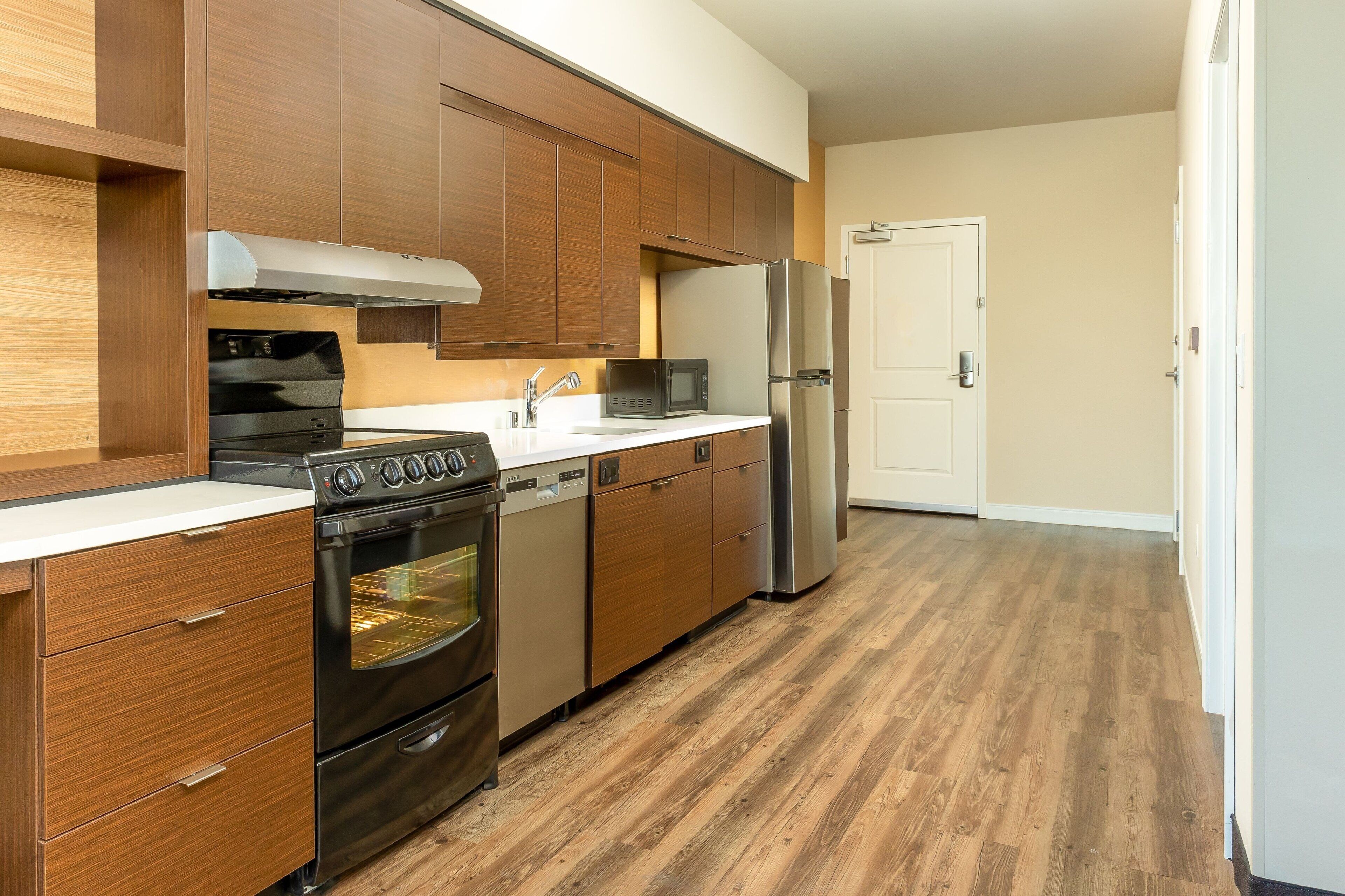 A compact kitchen with wooden cabinets, stainless steel appliances, and a wooden floor.