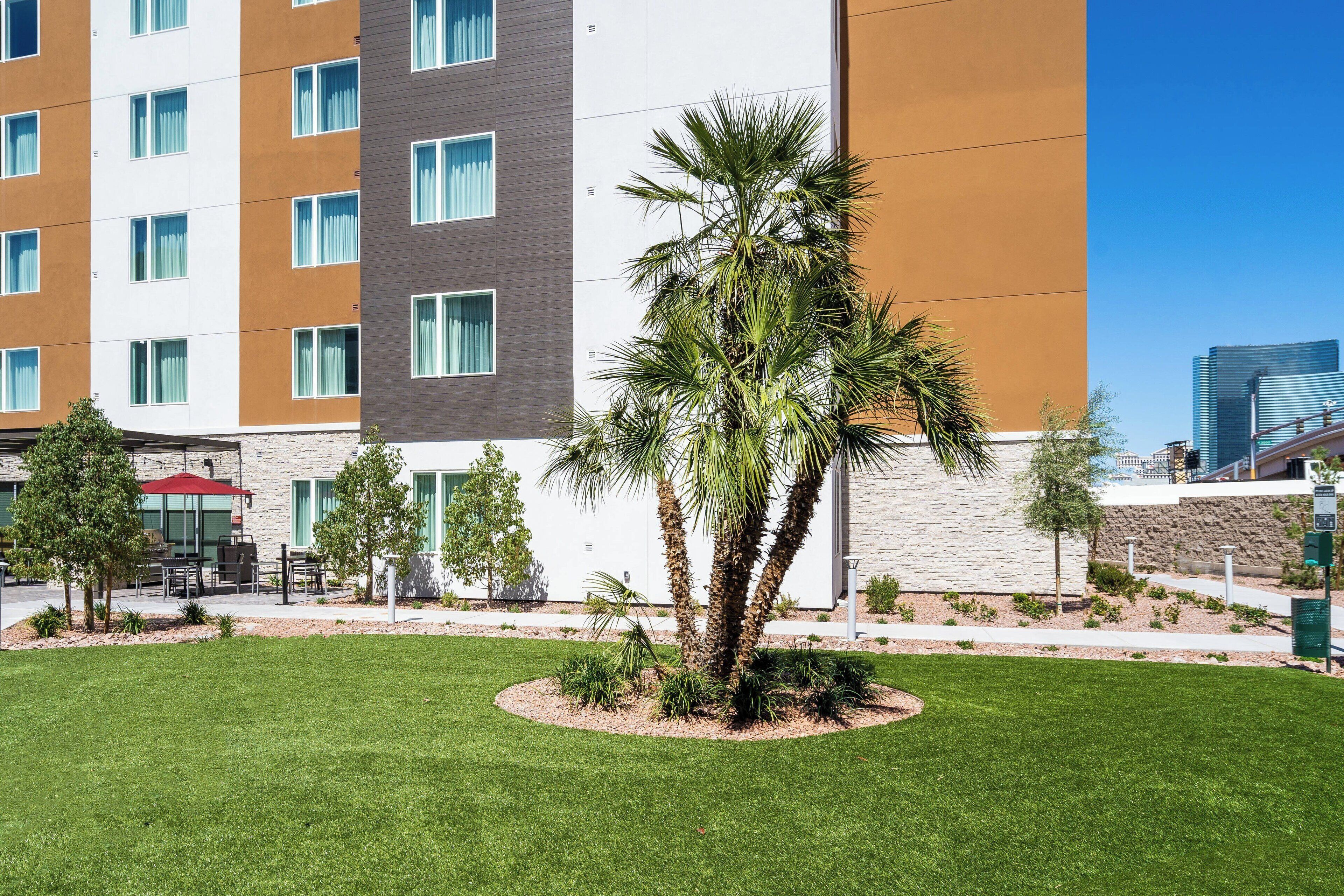 A modern hotel with a central courtyard featuring palm trees and a well-maintained lawn.