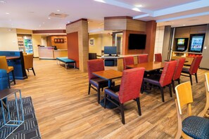 A hotel lobby with a reception desk, seating area with tables and chairs, a TV screen, and vending machines. - TownePlace Suites By Marriott Las Vegas Stadium District (Las Vegas)