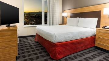 A hotel room with a large bed, a TV, a window with a city view, and a wooden headboard.