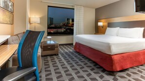 A hotel room with a bed, desk, chair, and a view of a cityscape through a window. - TownePlace Suites By Marriott Las Vegas Stadium District (Las Vegas)