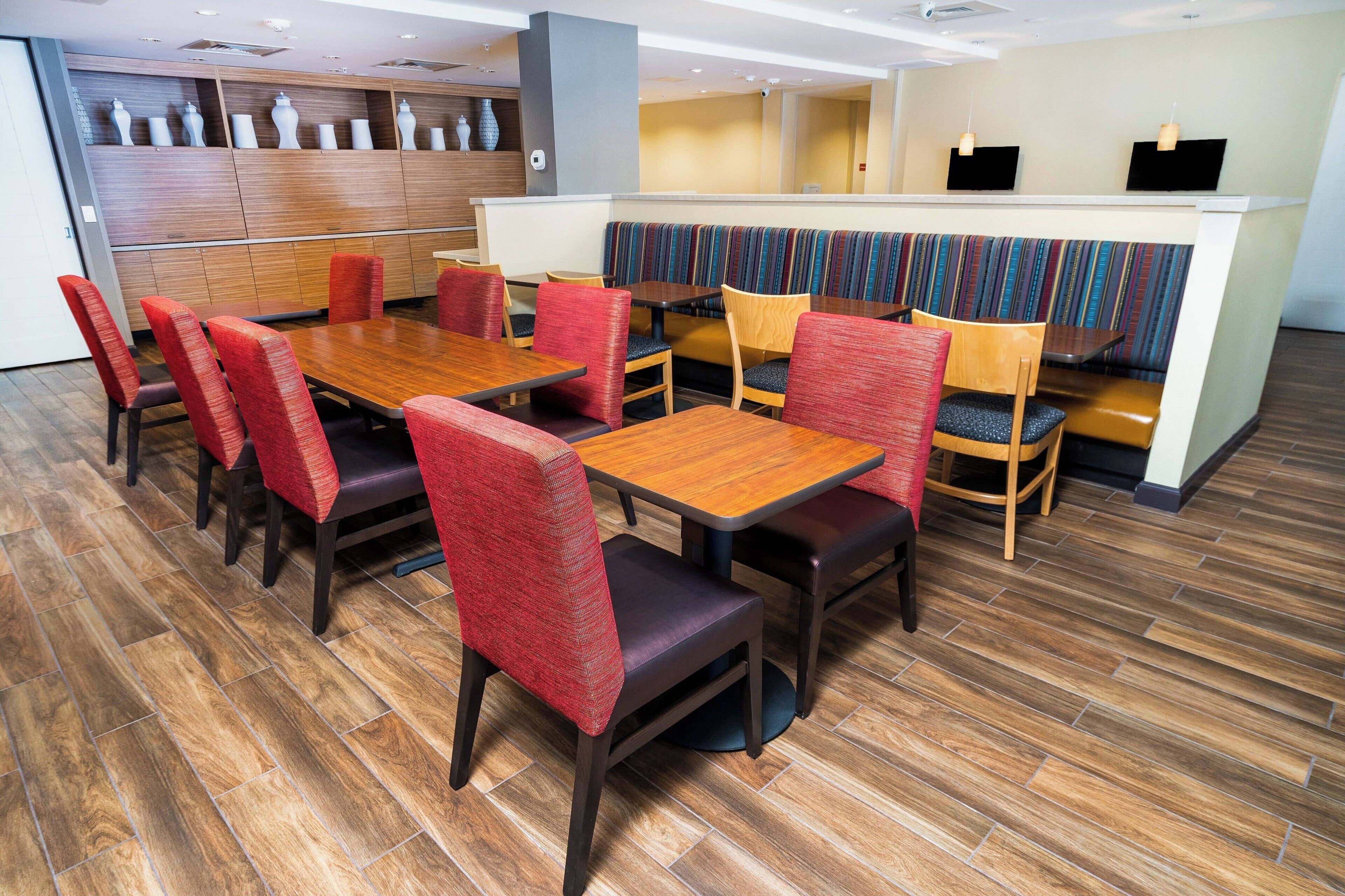 A modern restaurant with wooden flooring, red and brown upholstered chairs, and a central dining table.