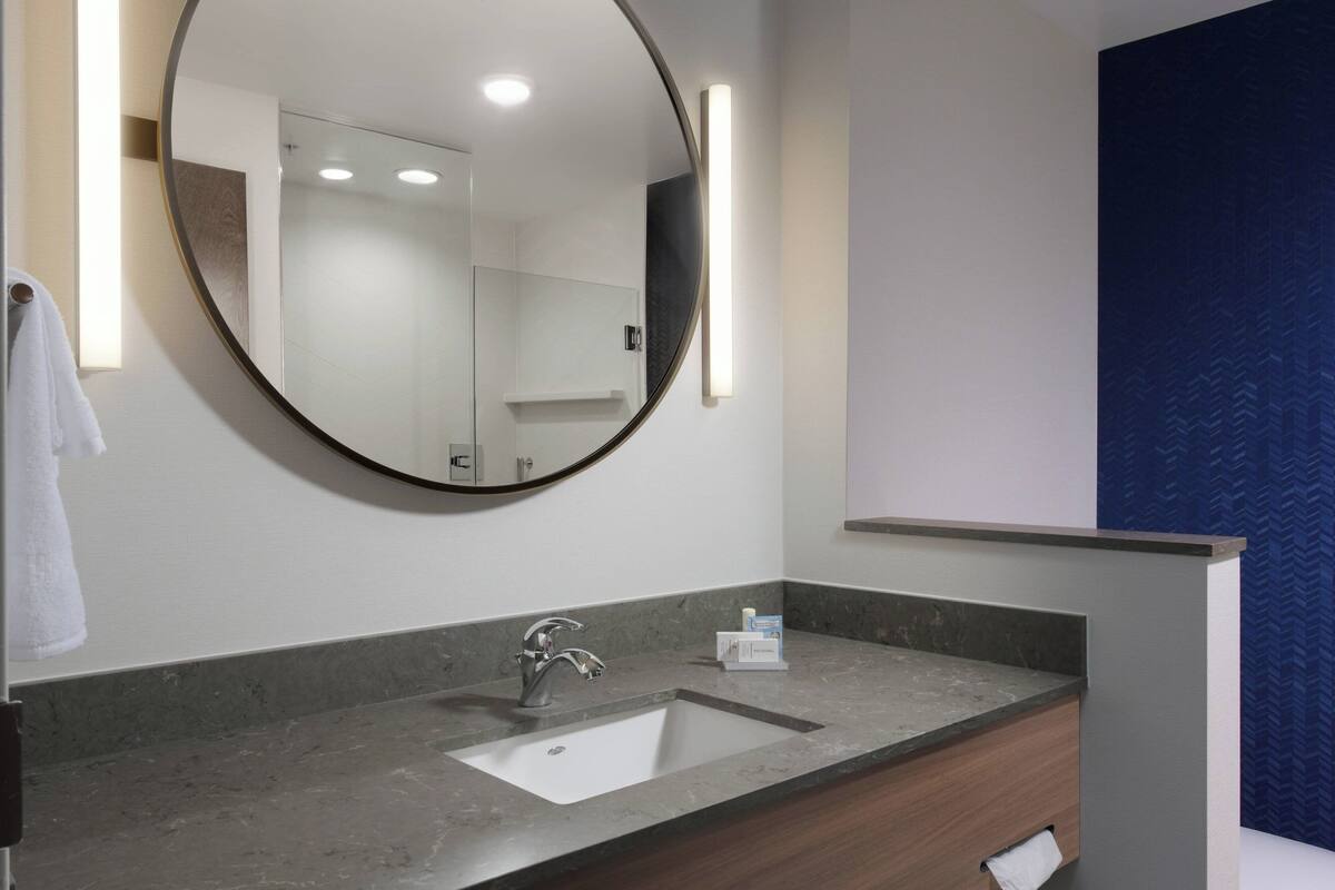 A bathroom with a round mirror, a sink, and a towel rack.