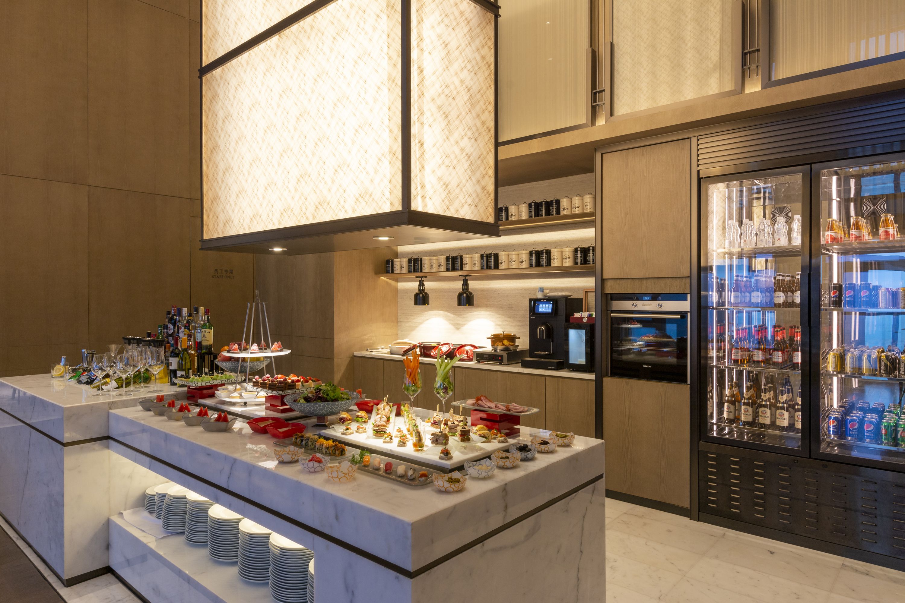 A buffet setup with various food items and beverages, a coffee machine, and a refrigerator stocked with drinks.