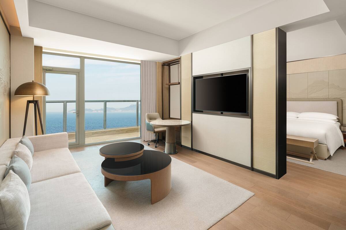 A modern hotel room with a sofa, a round table, a TV, and a bed.