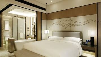A modern hotel room with a large bed, a bedside table with a phone, a wall-mounted artwork, and a bathroom visible through an open door.