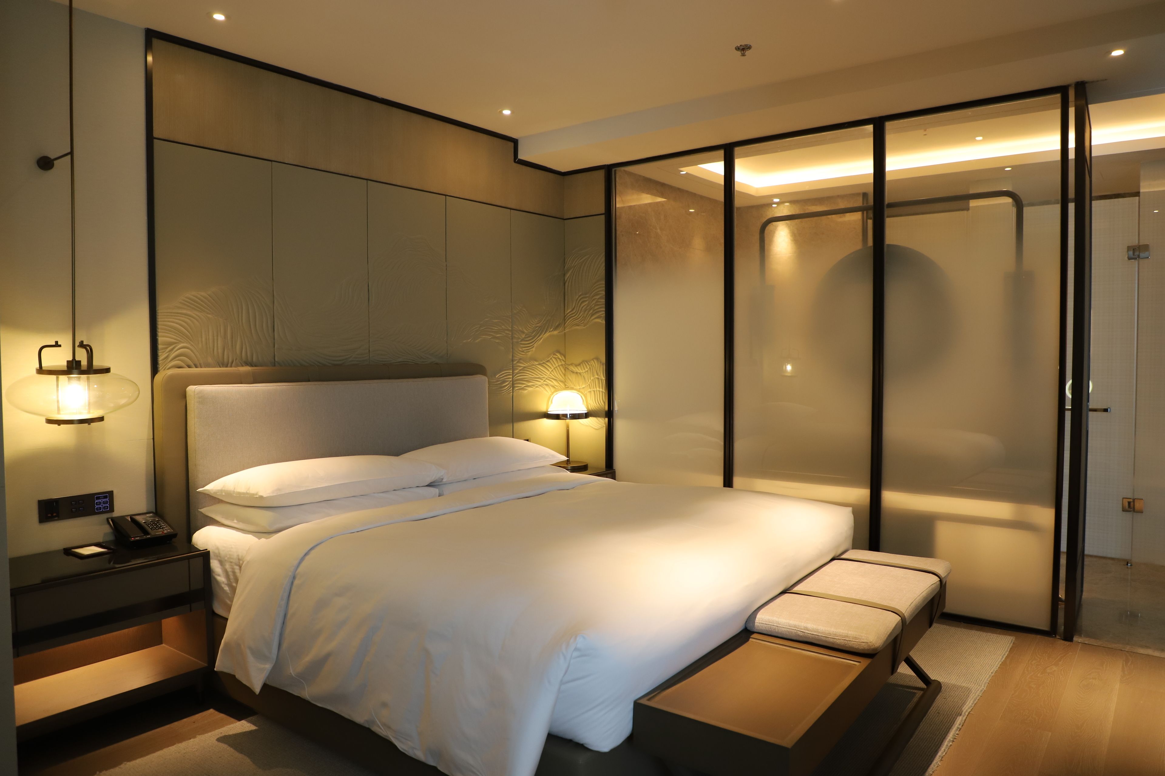 A modern hotel room with a large bed, bedside tables, a desk, and a walk-in closet.