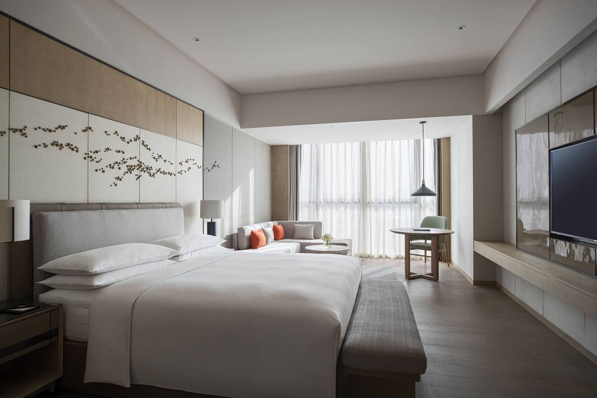 A modern hotel room with a large bed, a sofa, a small table, and a TV.