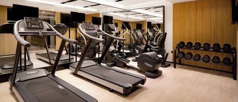 Un gimnasio moderno con cintas de correr, elípticas y un estante con mancuernas.
