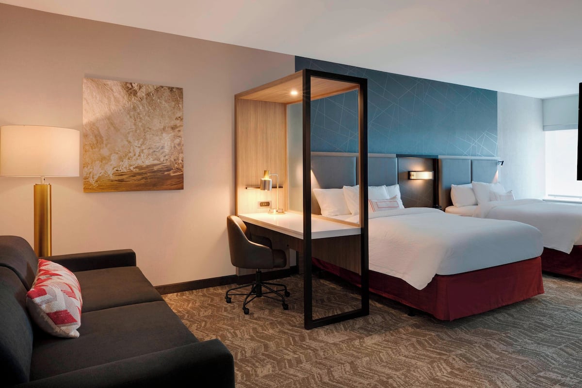 A hotel room with a bed, a desk, a chair, a sofa, and a painting on the wall.