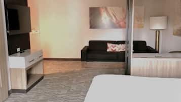 A modern hotel room with a large bed, a flat-screen TV mounted on the wall, a sofa, and a desk with a lamp.