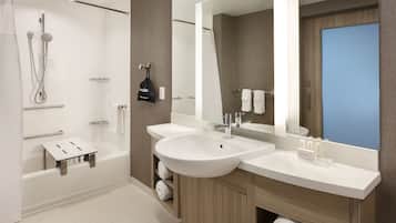 A modern bathroom with a bathtub, two sinks, a shower, and a large mirror.