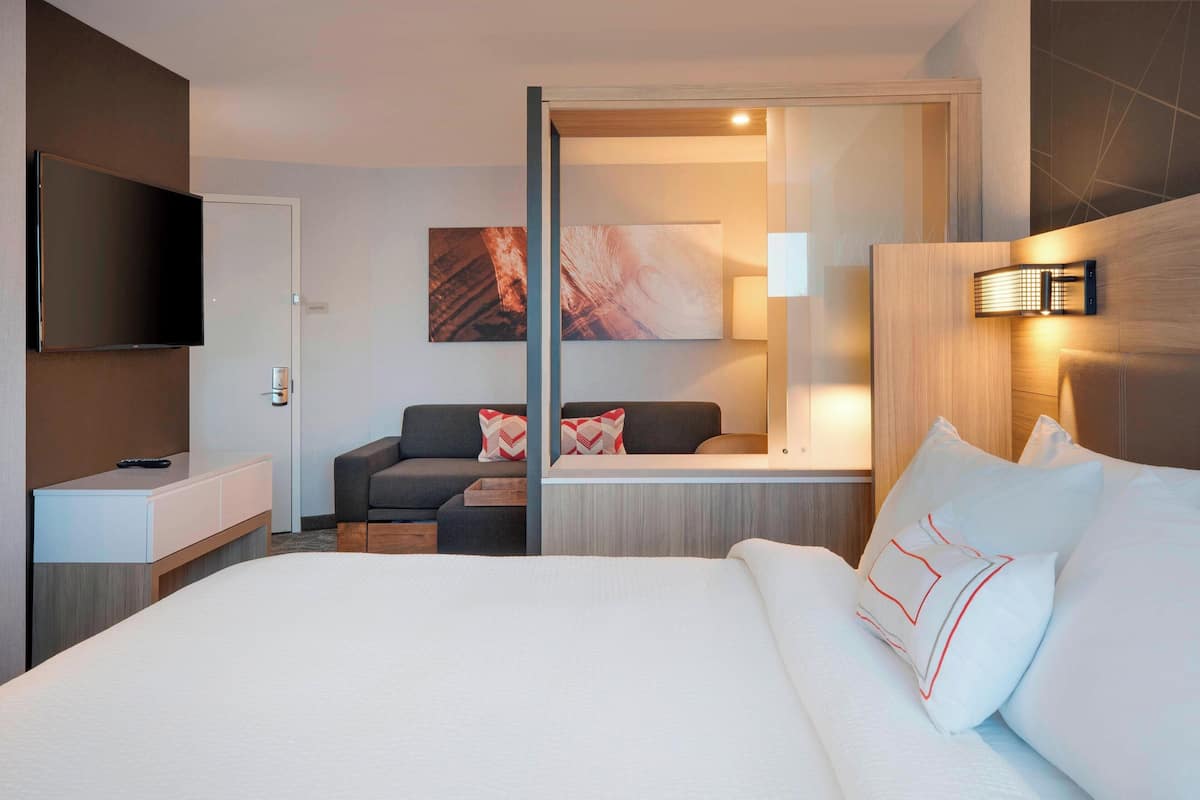 A hotel room with a large bed, a sofa, a TV, and artwork on the walls.