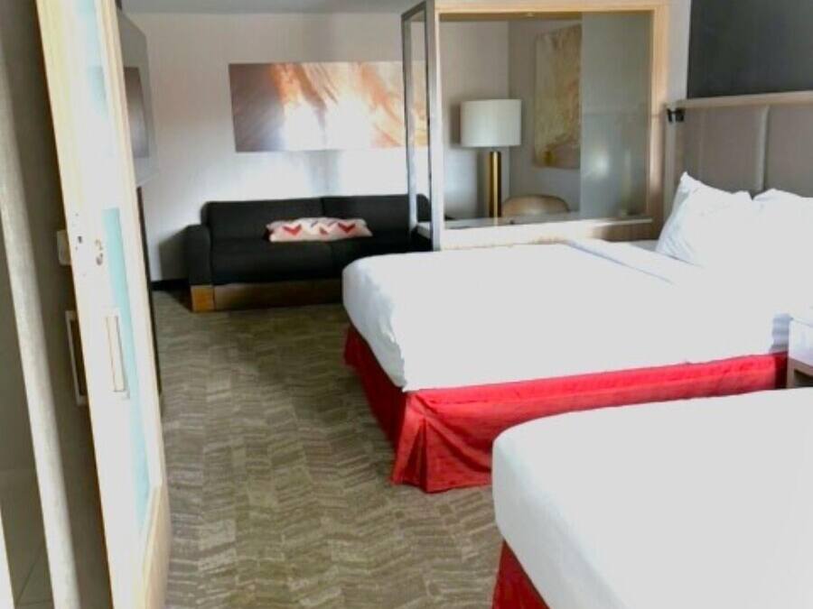 A hotel room with two beds, a sofa, a lamp, and a painting on the wall.