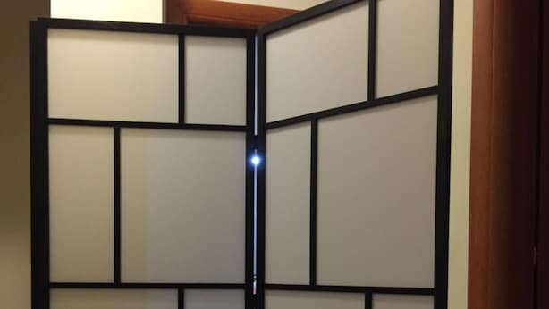 Una habitación con un panel divisor corredizo, suelo de madera y una puerta a la derecha.
