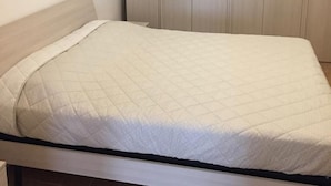 Una cama individual con colchón acolchado, cabecero de madera y una pared lisa con un panel de madera en la parte superior.