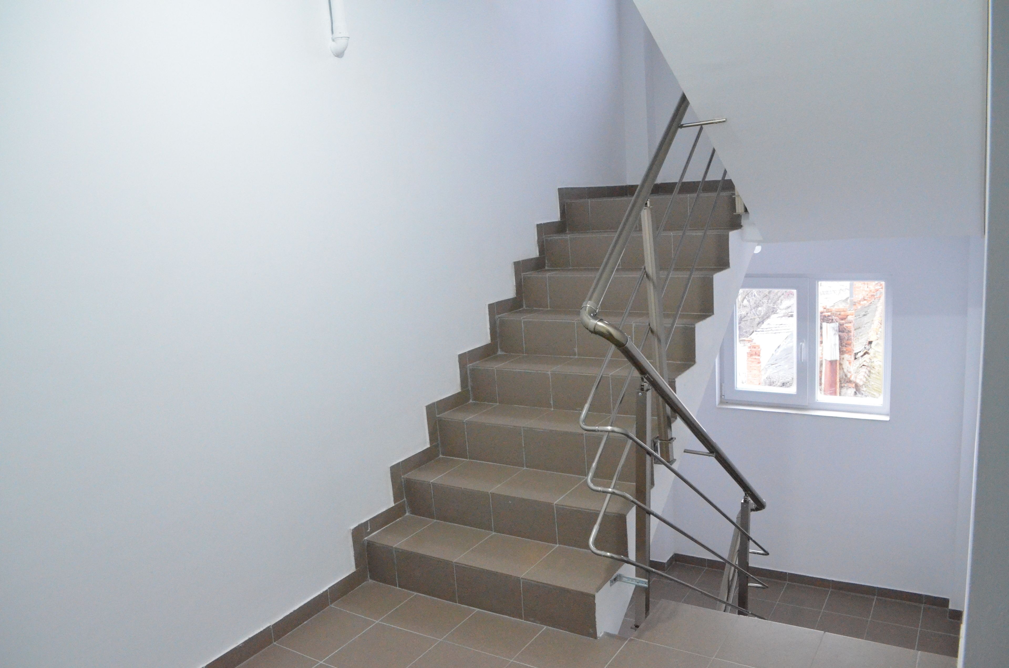 A staircase with a metal handrail and beige tiles.