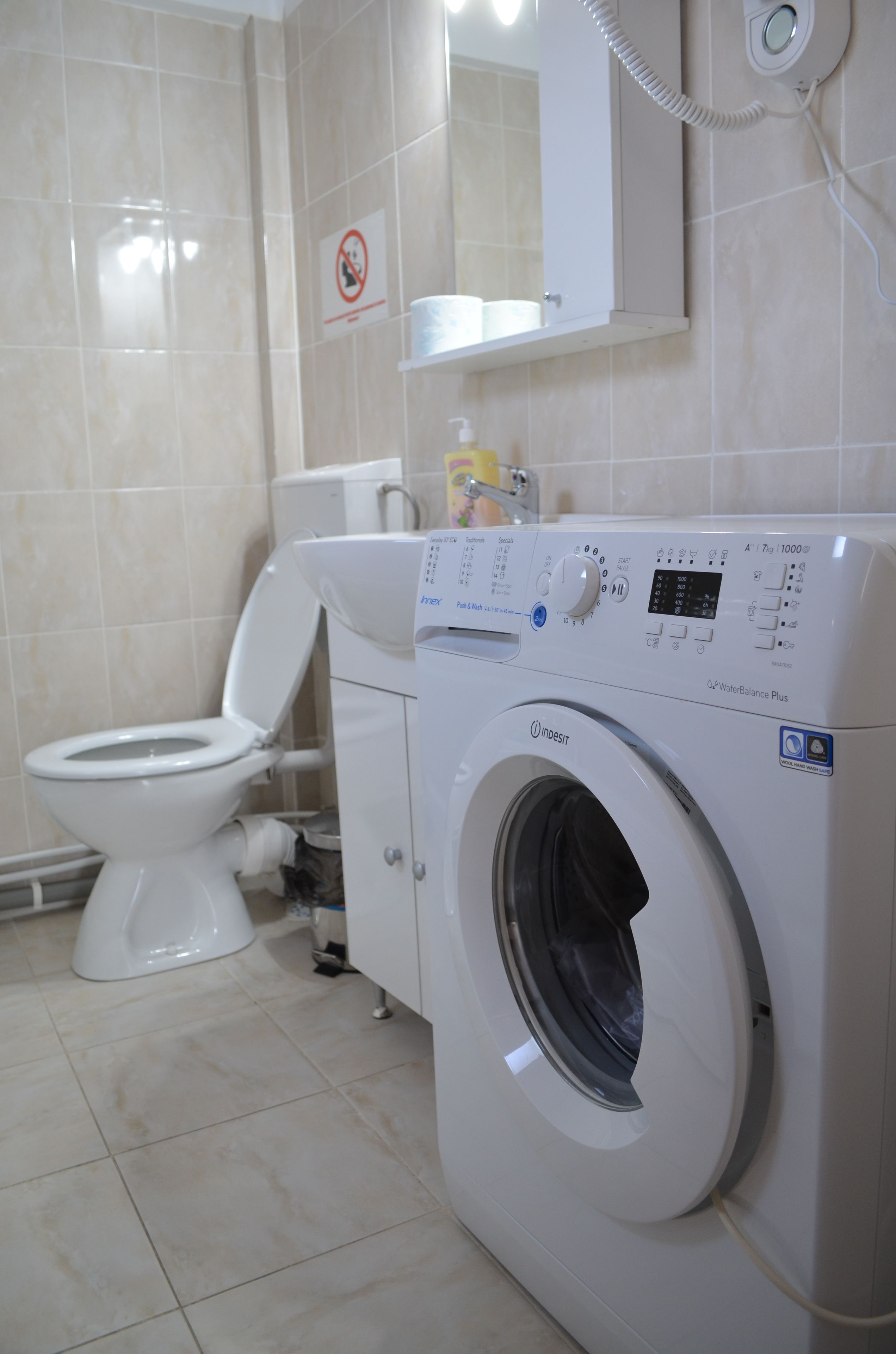 Un baño moderno con inodoro blanco, lavadora y un cartel de prohibido fumar en la pared.